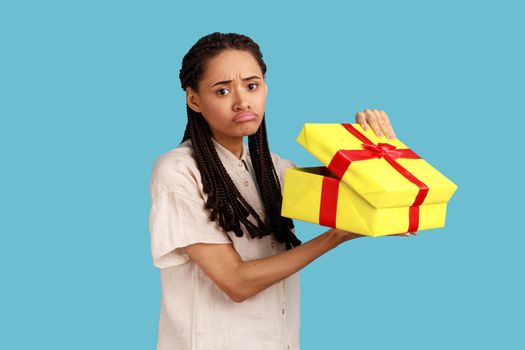 Woman with black dreadlocks looking into gift box, opening present and looking at camera with sorrow