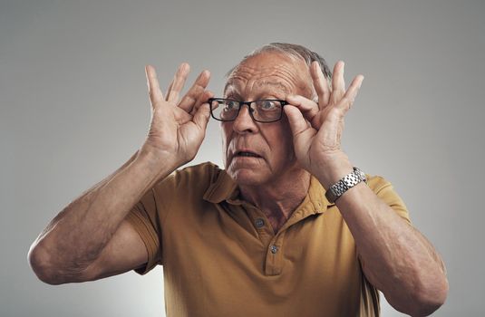 Like my new specs. Studio shot of an elderly man adjusting his spectacles against a grey background.
