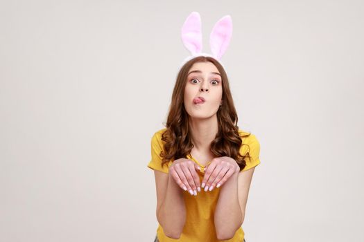 Portrait of happy woman of young age in yellow T-shirt with bunny ears and making hare paws with hands, childish grimace, humorous expression.