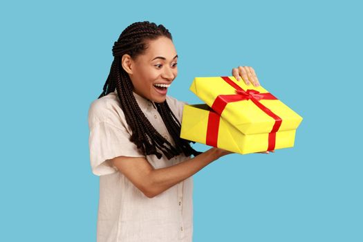 Woman with dreadlocks looking into gift box, opening present and peeking inside with happiness.