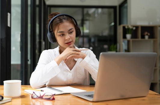 Online education, e-learning. young woman studying remotely, using a laptop, listening to online lecture, taking notes while sitting at home, smiles