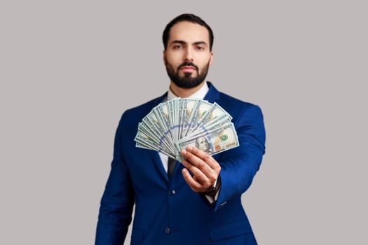 Self confident rich bearded man holding out dollar bills at camera, boasting money won in lottery.