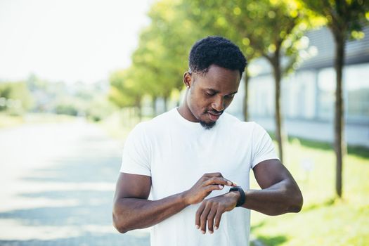 Young african american man, on a morning jog in a white t-shirt in the park, switches