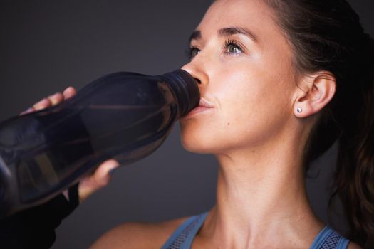 Hydration is key for peak performance. a sporty young woman drinking water against a grey background.