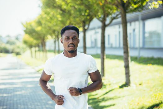 A young African American man, on a morning jog in a white T-shirt in the park