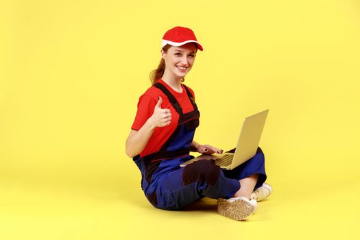Optimistic worker woman sitting on floor with crossed legs and working on notebook, showing thumb up