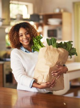 Healthy living begins at home. Portrait of a happy young woman holding a bag full of healthy vegetables at home.