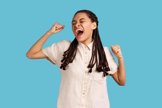Woman with black dreadlocks yawning and raising hands up, feeling fatigued, standing with close eyes
