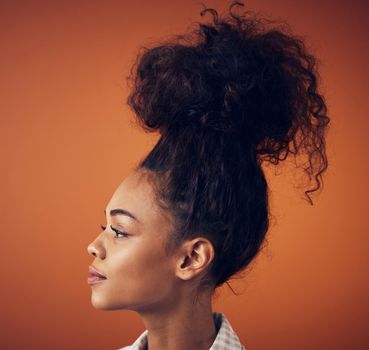 The bigger the bun, the bigger the dreams. a young woman wearing her hair in a bun against an orange background.