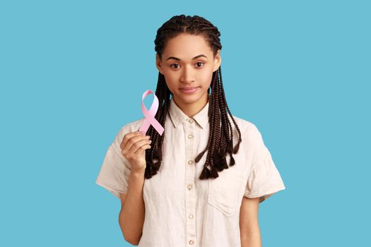 Positive woman with black dreadlocks holding pink ribbon, symbol of breast cancer awareness.