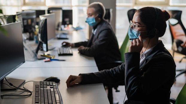 Two women in medical masks and headsets are working in the office