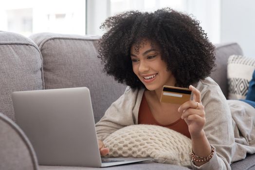 Pay day. a young woman shopping online while laying on the couch at home.