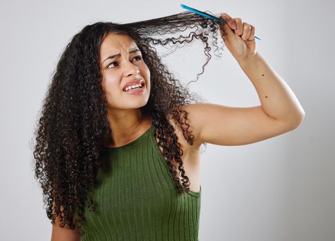 Combing out my hair is never an easy task. a woman frowning while combing her hair against a grey background.