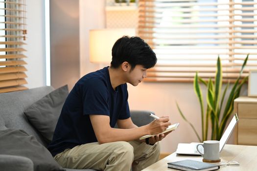 Side view asian male freelancer working online with laptop computer on couch at home