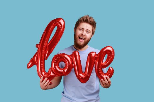 Man in blue T-shirt holding love word of foil balloons expressing positive emotions and his feelings