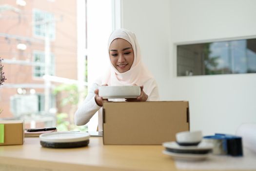 Muslim female online store small business owner seller entrepreneur packing package post shipping box preparing delivery parcel on table. Ecommerce dropshipping shipment service concept