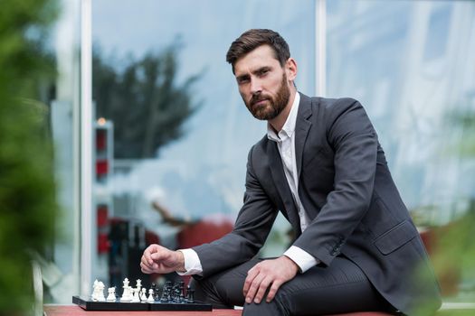 Successful man sitting on a bench in a business suit playing chess, and looking thoughtfully