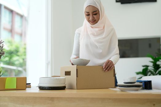 Muslim female online store small business owner seller entrepreneur packing package post shipping box preparing delivery parcel on table. Ecommerce dropshipping shipment service concept.