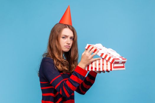 Upsety woman holds present box, being disappointed with gift, looking at camera with sad expression.