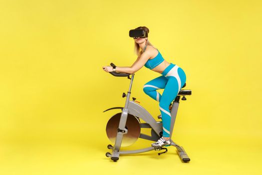 Athletic sporty woman pedaling on exercise bike looking through augmented reality viewer.