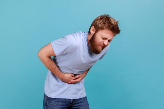 Man in T-shirt stands and holding his painful belly, feeling bad, suffering diarrhea or constipation
