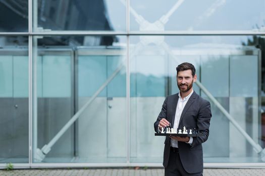 Successful and happy businessman looking at camera and holding chessboard