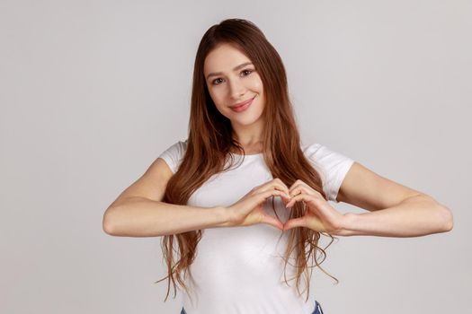 Lovely romantic happy woman making heart shape with fingers, gesturing love hope charity sign.