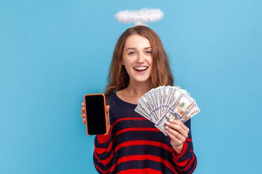 Woman with nimb over head showing smart phone with blank screen and dollar banknotes.