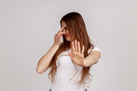 Woman pinching nose with fingers to avoid bad smell and showing stop gesture, grimacing with disgust