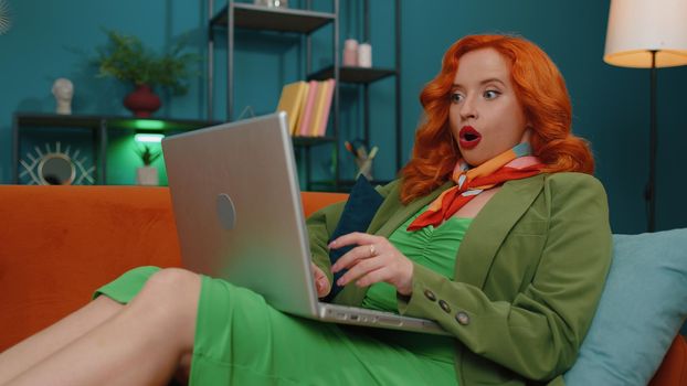 Amazed ginger girl use laptop computer, receive good news message, shocked by victory, celebrate win