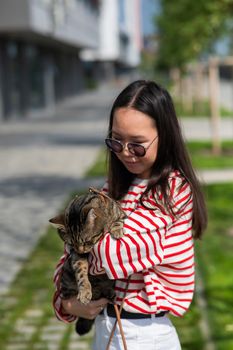Young woman holding tabby cat in her arms outdoors.