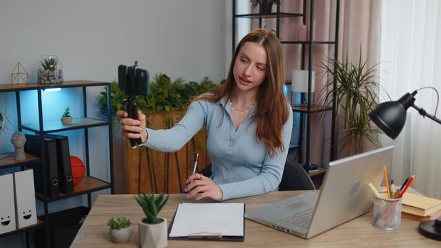 Young woman businesswoman blogger using smartphone shooting video call for social media posing smiling sitting at table working from home office. Girl freelancer study, e-learning, remote job online