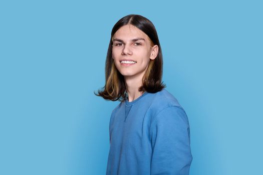 Headshot portrait of teenage guy looking at camera on blue background