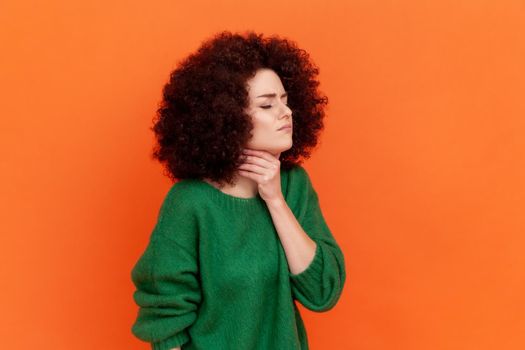 Profile portrait of young adult woman with Afro hairstyle wearing green casual style sweater having sore throat, touching neck, feels bad.
