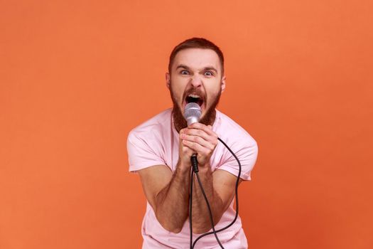 Man holding microphone in hands, looking at camera and screaming loudly.
