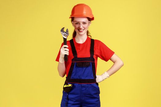 Builder woman holding adjustable wrench, looking at camera with happy facial expression.
