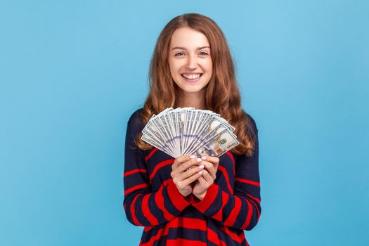 Woman holding fan of dollar bills and looking ar camera with toothy smile, lottery winner.