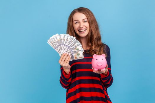 Woman holding fan of dollars banknotes and piggy bank, profitable conditions for saving money.