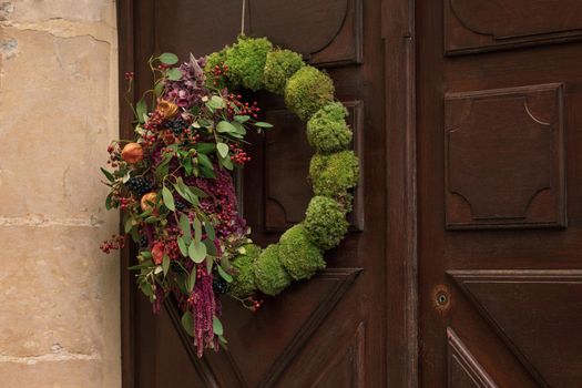 Wreath with the red berries and dry leaves hanging on a door.