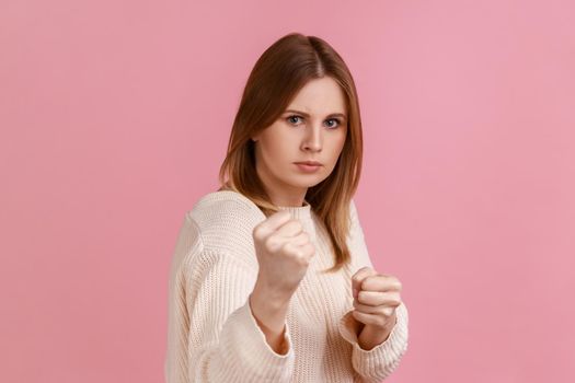 Confident attractive blond woman clenching fists, showing boxing gesture and ready to punch.