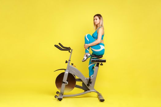 Attractive woman instructor stretching leg before training on exercise bike, looking away.