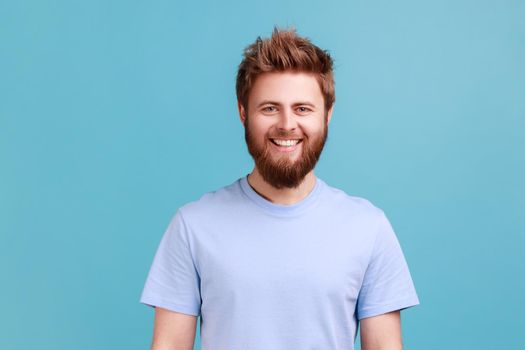 Man in blue T-shirt looking at camera with toothy smile and happy expression, being in good mood.