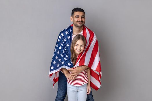 Father and daughter standing wrapped in big flag of United States of America together.