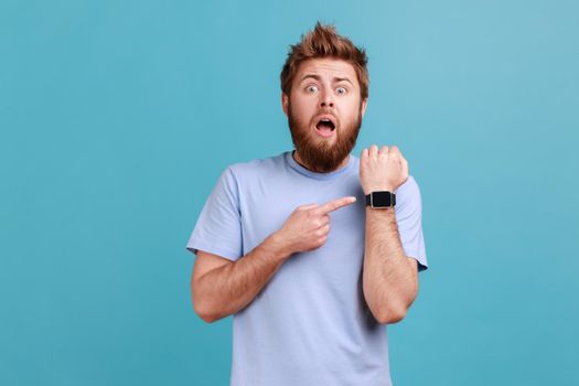 Man with open mouth and wondered astonished expression, pointing with finger ar smartwatch.