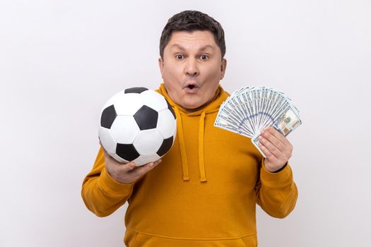 Surprised middle aged man showing soccer ball and fun of hundred dollar bills, betting for sport.