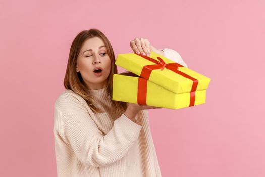 Attractive young blond woman loooking inside yellow present box, being interested what inside.
