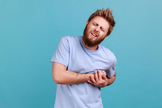 Man in blue T-shirt suffering sudden heart attack or painful cramps, cardiac problems, frowning face