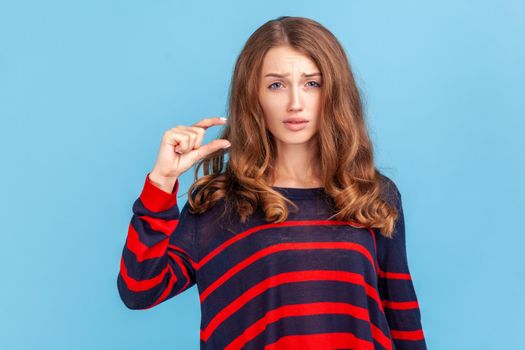 Too small. Portrait of dissatisfied woman in striped casual sweater showing a little bit gesture, inch or centimeter, disappointed with minimum size.