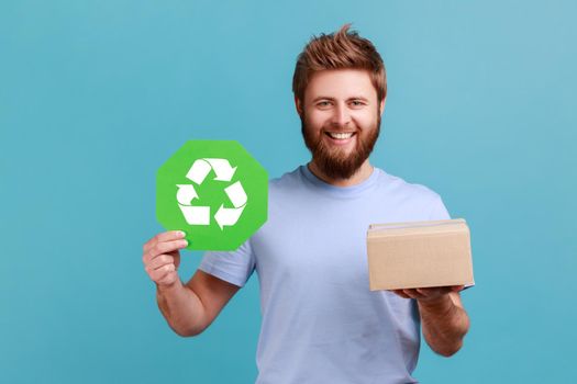 Man in T-shirt holding green recycling sign and cartoon package, looking at camera with toothy smile