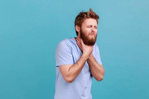 Man in blue T-shirt grimacing touching his neck, feeling pain while swallowing, sore throat.